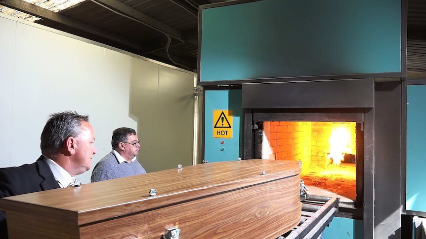 Two men load a coffin into be cremated