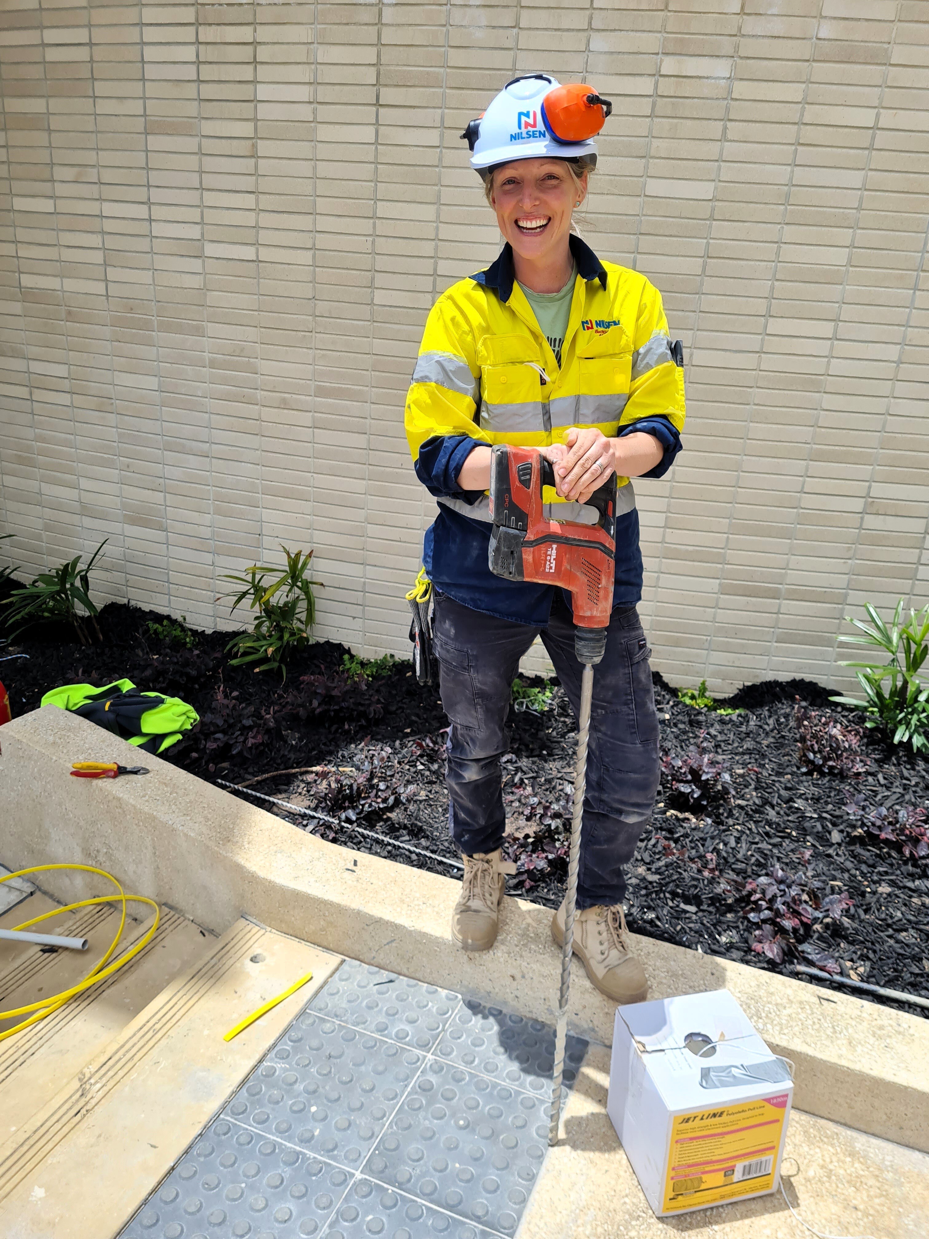 A woman wearing a hard hat and a high visibility shirt holding a drill