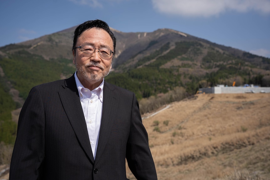 A Japanese man in a suit stands on a hillside