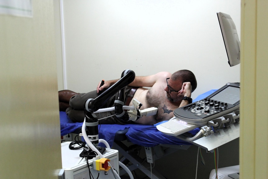 A robot scans a man's chest while he lays on his side
