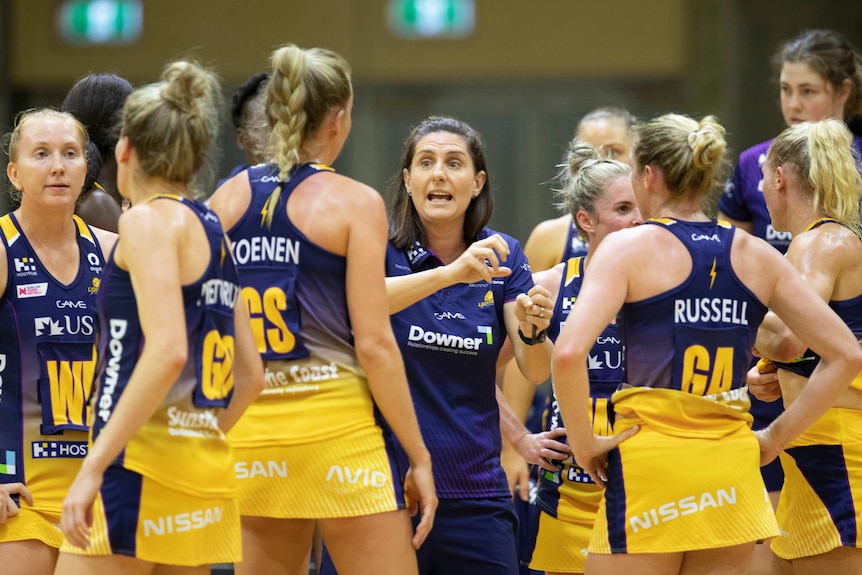 A netball team surrounds its coach while they listen to her talk.
