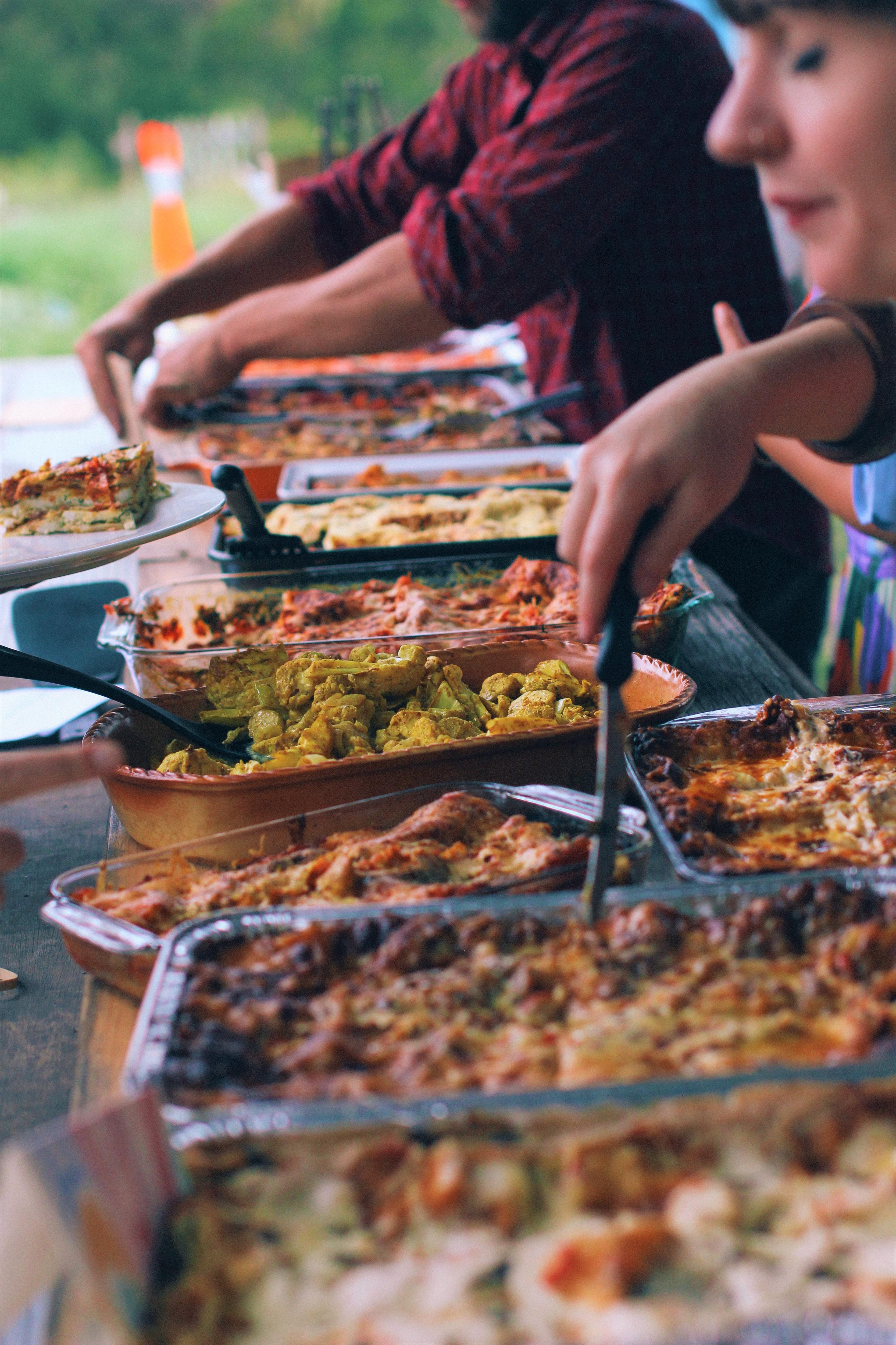 A row of lasagnes on a table with hands reaching in holding a spatula to serve it