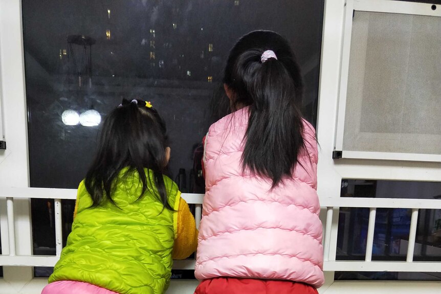 Hui Qiu's daughters look out the window from the apartment they are staying in in Wuhan, China, amid the coronavirus lockdown.