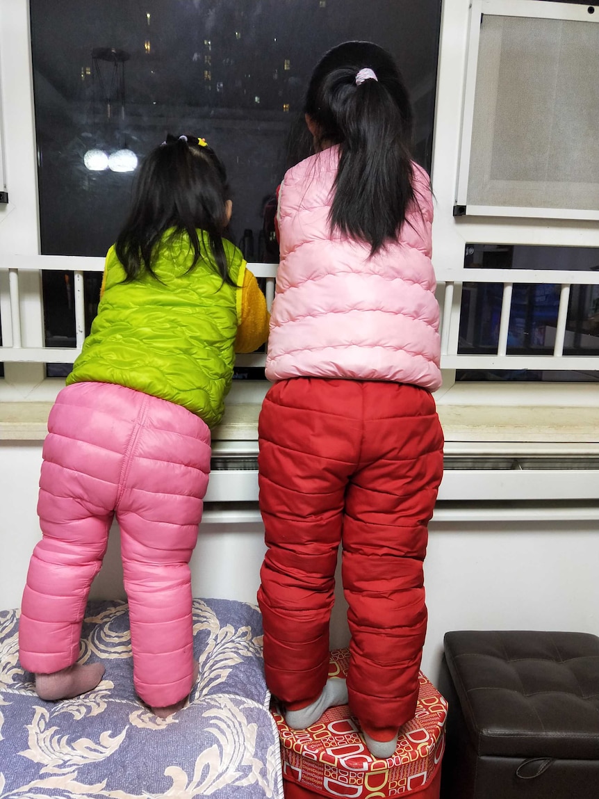 Hui Qiu's daughters look out the window from the apartment they are staying in in Wuhan, China, amid the coronavirus lockdown.