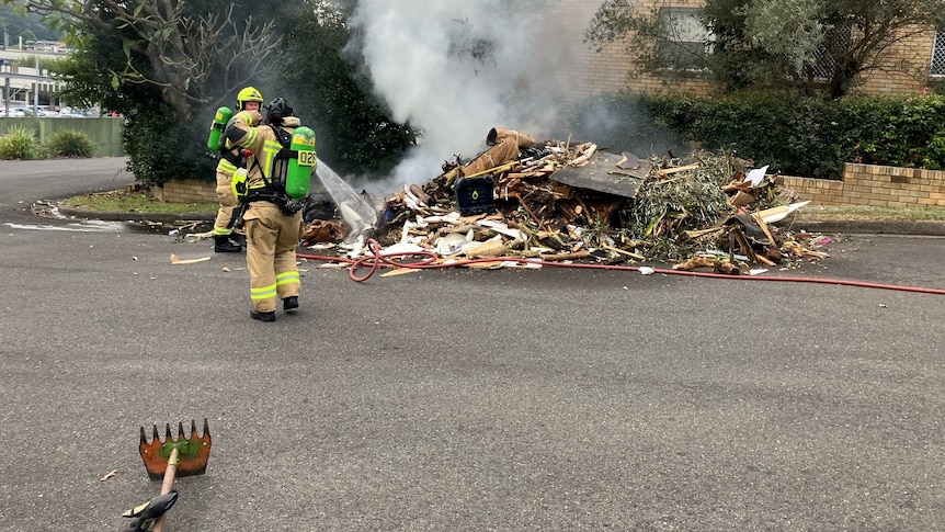 Firefighters attend a smoking pile of rubbish.
