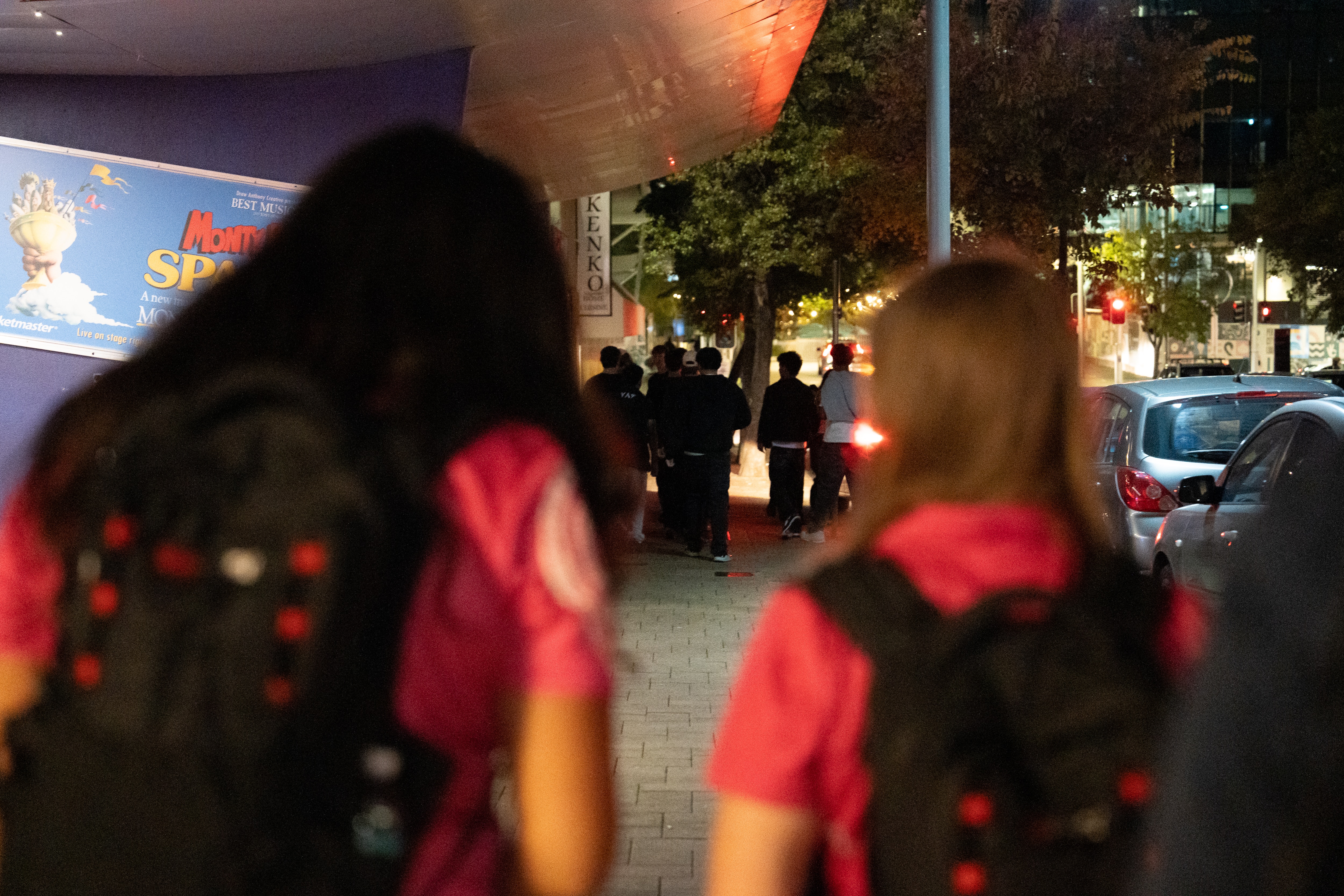 Two youth workers blurred in the foreground walk behind a group of young people in perth's CBD at night.