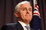 Malcolm Turnbull frowns during a press confernce, standing at a microphone in front of an Australian flag.