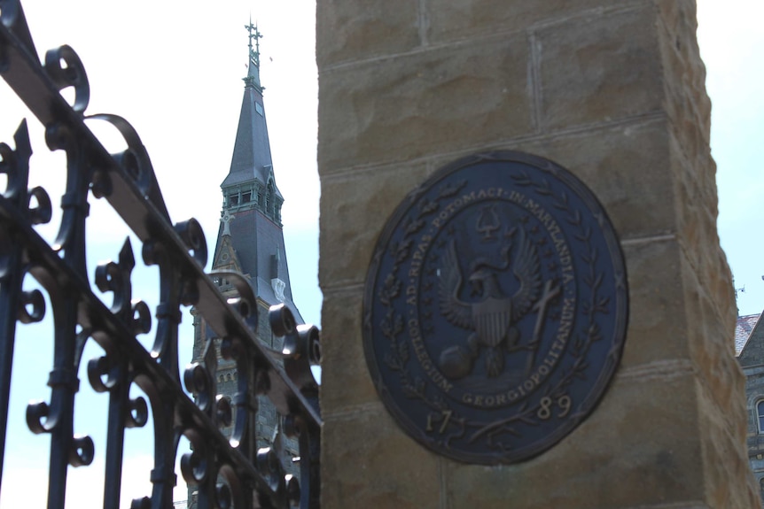 The logo to Georgetown University in Washington DC on a column, with a spire in the background.