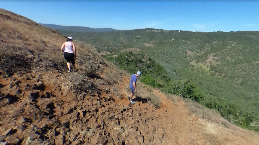 Two people in gym clothes walk on a rocky mountainside.