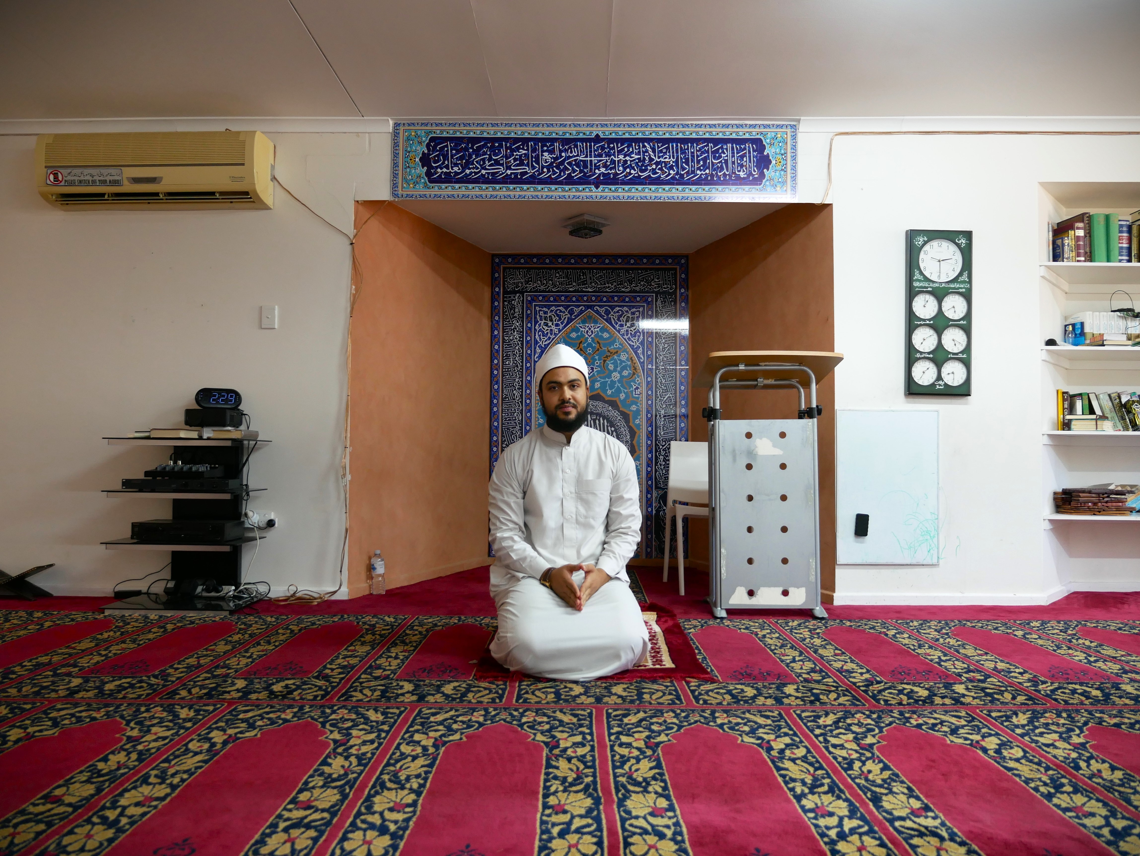 A Muslim man in white traditional dress sits on his knees inside the Alice Springs Mosque.