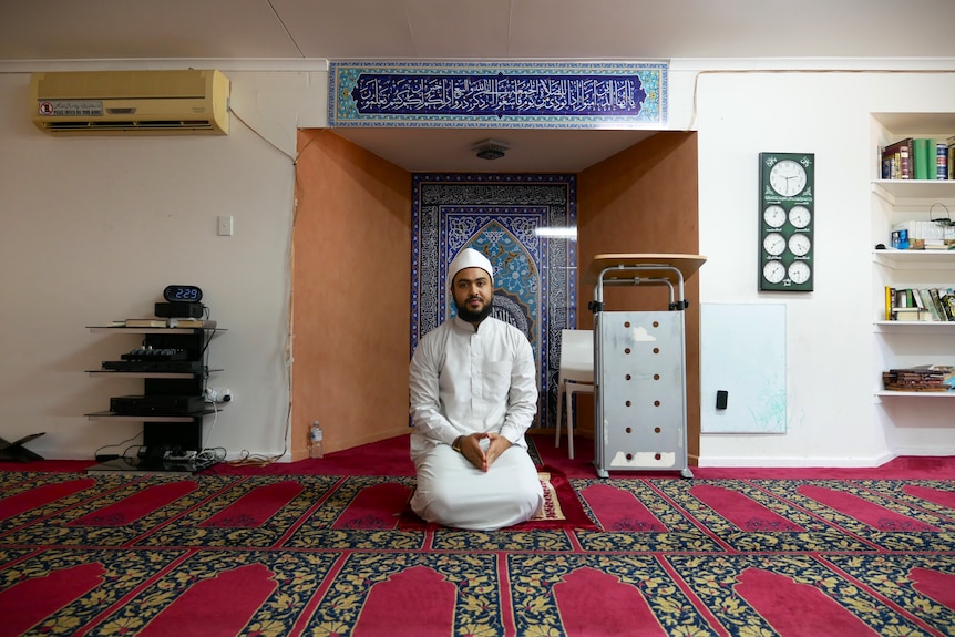A Muslim man in white traditional dress sits on his knees inside the Alice Springs Mosque.