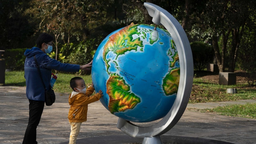 A woman and her child, wearing masks to protect from the coronavirus, look at a giant globe