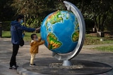 A woman and her child, wearing masks to protect from the coronavirus, look at a giant globe