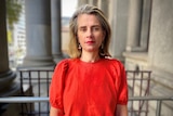 A woman in a red shirt stands in front of grey pillars