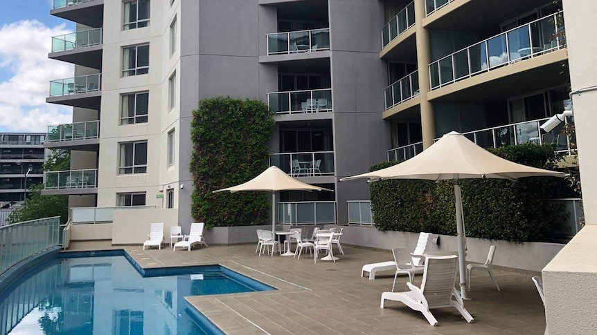 A hotel with a pool under a cloudy sky.