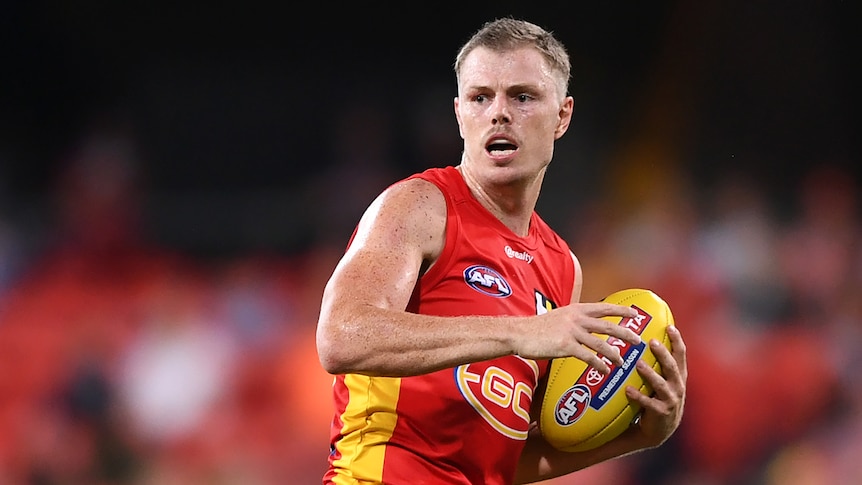 A Gold Coast Suns player holds the football as he considers where to kick it next during a game.