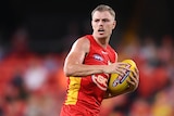 A Gold Coast Suns player holds the football as he considers where to kick it next during a game.