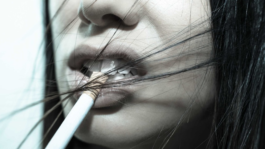 A close up of a cigarette hanging from a young woman's mouth.