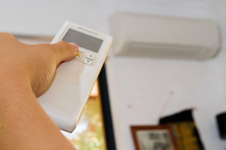 A hand holding an air-conditioner remote control.