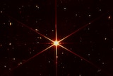 A red star with six lines coming out from the center with other galaxies and stars surrounding it.