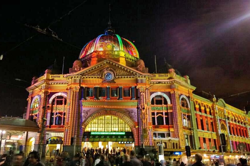 The front of Flinders Street Station is lit up with different colours.