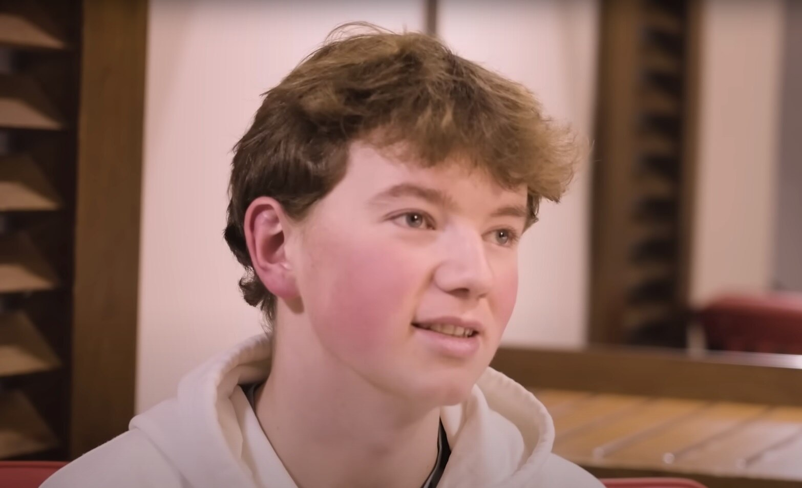 Image of a teenager wearing a white hoodie. He is looking out of frame. 