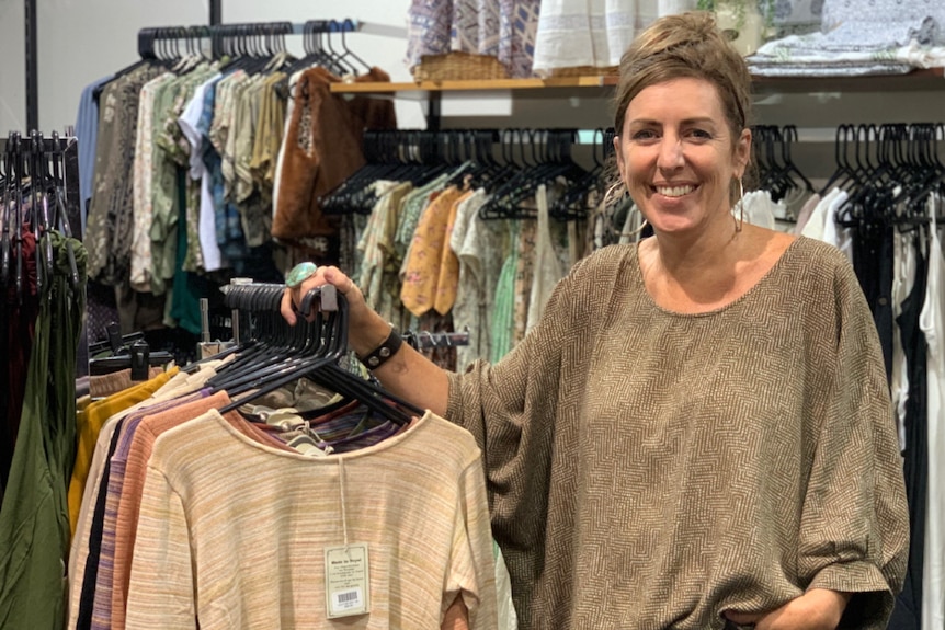 Woman standing in a clothing shop, smiling.