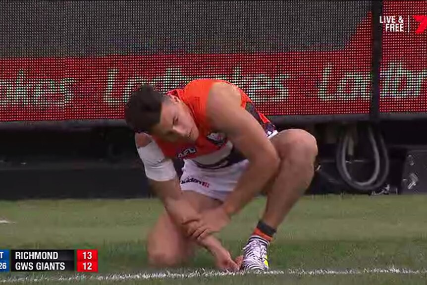 A TV still of Dylan Shiel holding his arm while kneeling in front of a Ladbrokes sign.