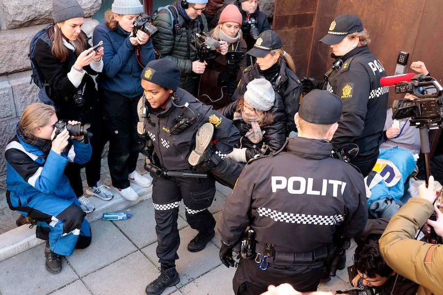 A woman is carried by police as people watch on holding cameras. 
