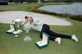 New Zealand LPGA golfer Lydia Ko lies on the grass and points to three trophies she has just won. 