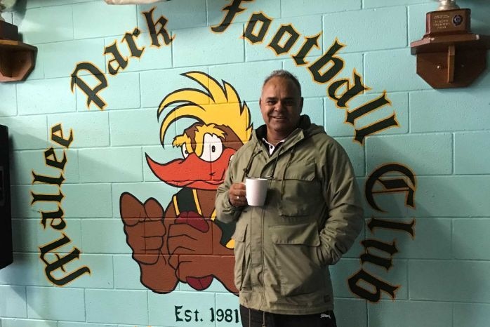 A man in a coat stands with a coffee cup in his hand into of a painted wall.