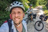 Kurt and his partner take selfie sitting on their bikes along a bike path 