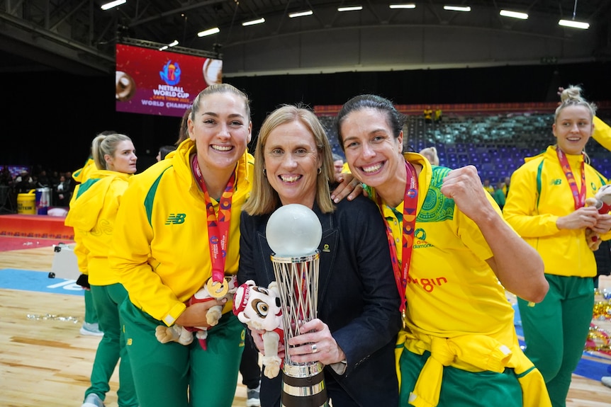 Sophie Garbin and Ash Brazill stand either side of their coach as they pose with the World Cup trophy