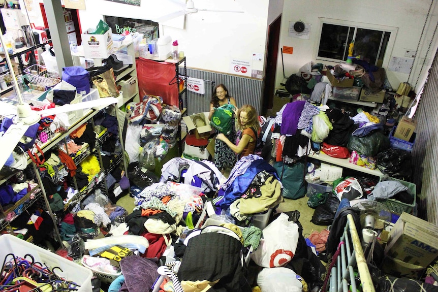 Two women going through a room full of clothes and household products.