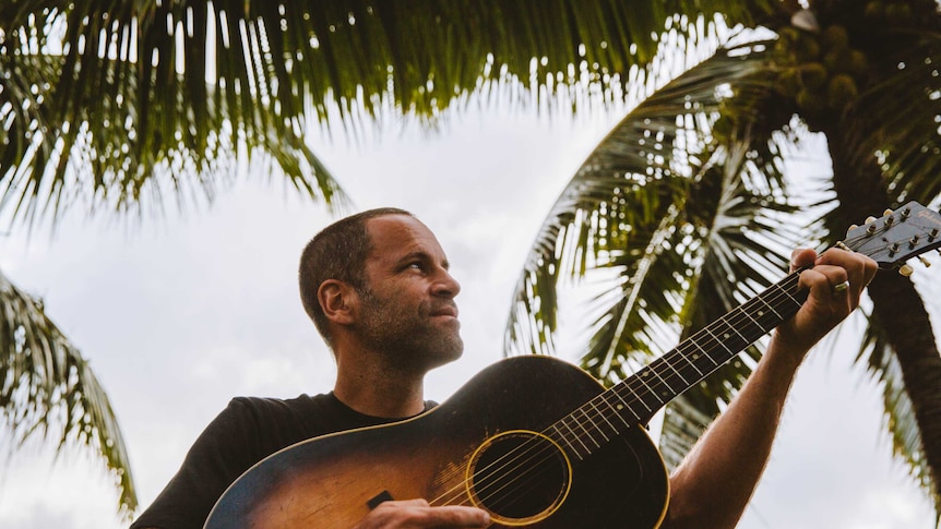 Jack Johnson with a guitar standing outside and looking away from the camera