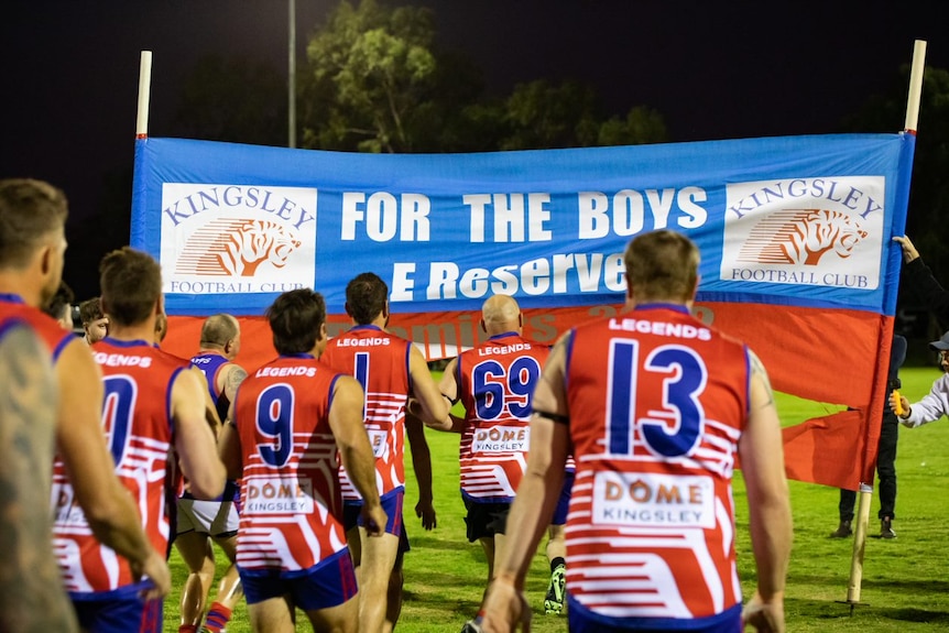 Players dressed in red, white and blue about to run through a banner that says "For the boys" 