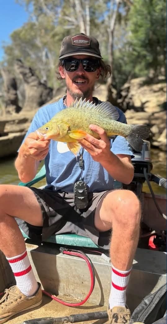 Man sitting in a boat wearing glasses and holding a fish