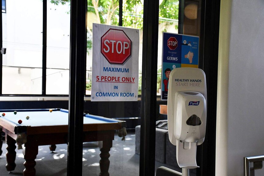 Hand sanitiser on door and sign of 5 people only inside the common area for boarders at Nudgee College.