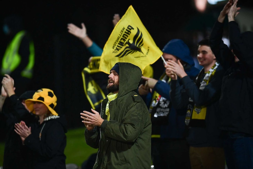 Wellington supporters stand and applaud, waving yellow flags