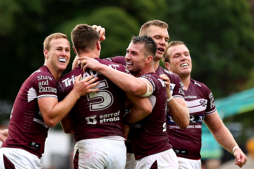 A group of NRL players pat their teammate on the head and back after he scores a try.