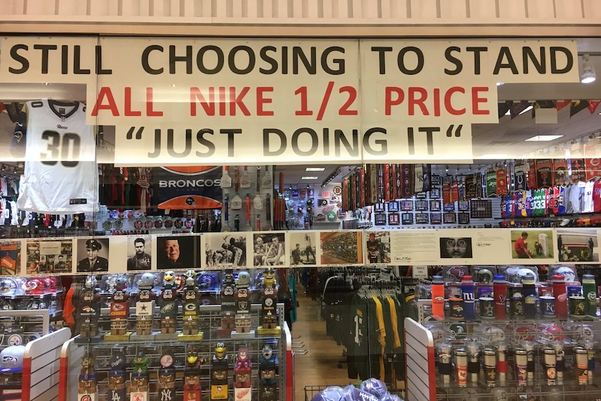 A sign saying "Still choosing to stand - All Nike 1/2 price" sits in a shop window.