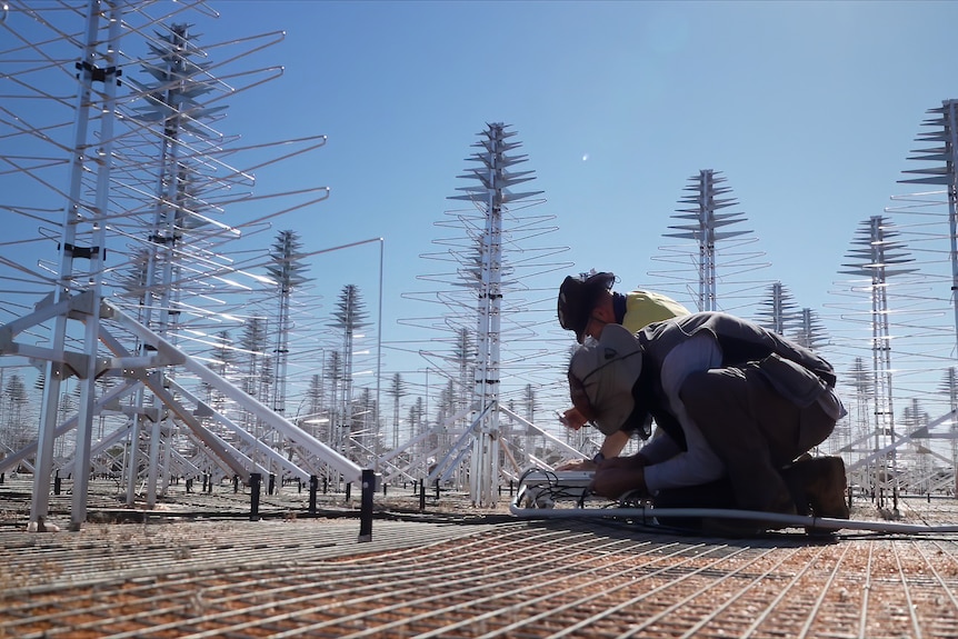 Two workers work on their knees to assemble an antenna.