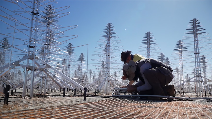 Two workers work on their knees to assemble an antenna.