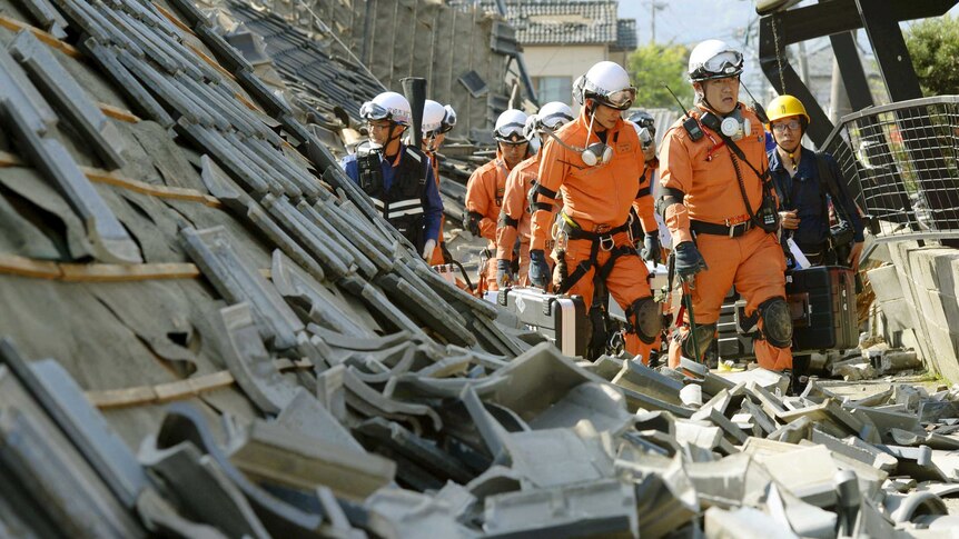 Firefighters walk among collapsed houses caused by an earthquake in Mashiki town.