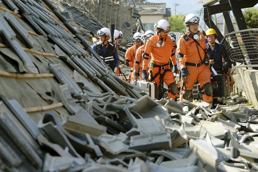 Firefighters walk among collapsed houses caused by an earthquake in Mashiki town.