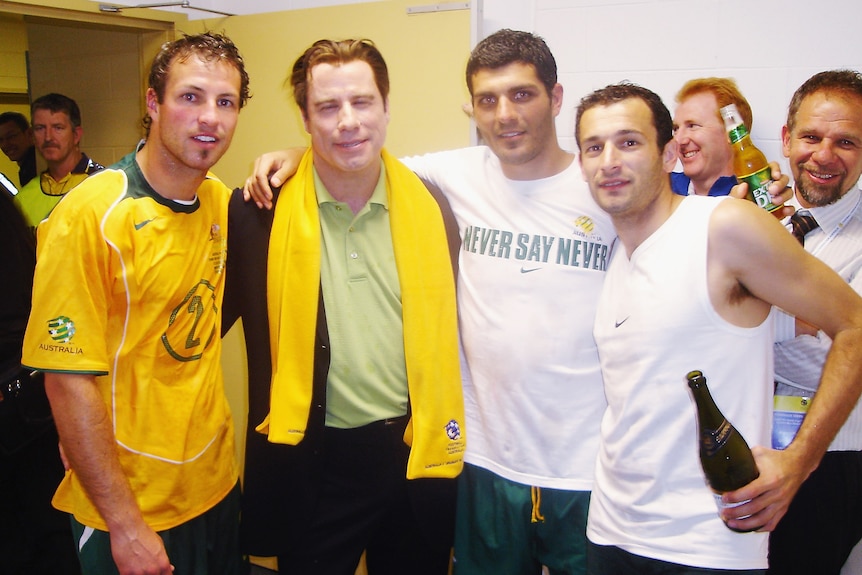 A group of men smiling with arms around each other in a change room dressed mostly in yellow