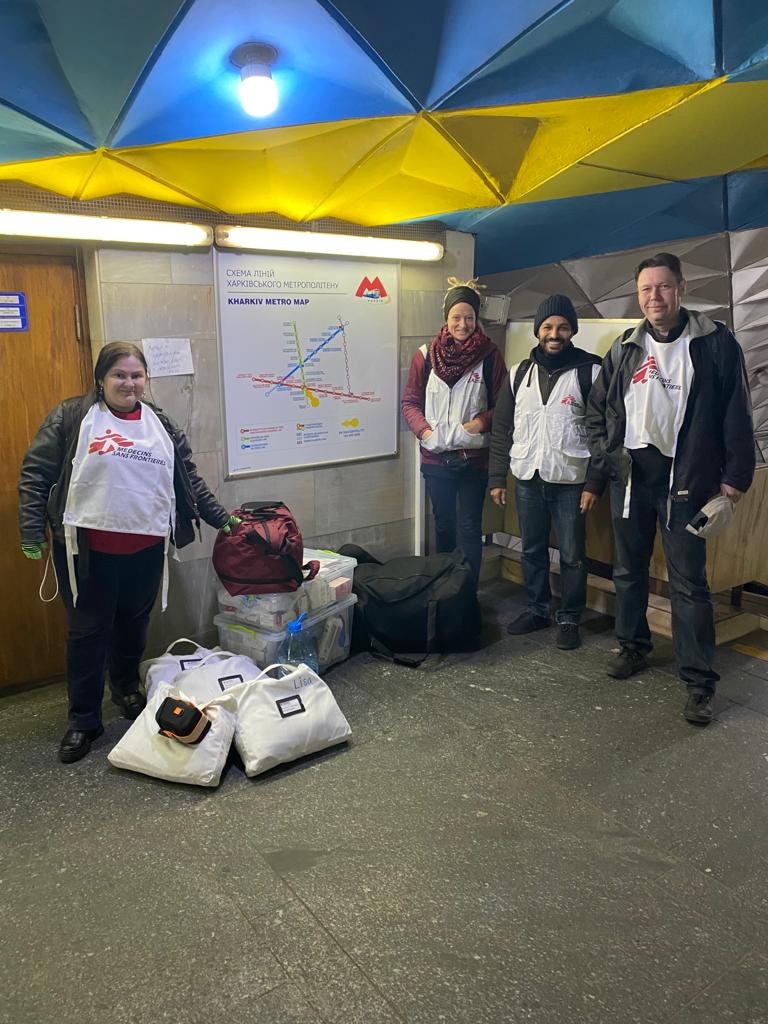 A group of people in beanies and white MSF vests poses for a photo in a metro station
