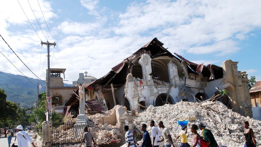 People carrying their belongings walk past the collapsed Sacre Coeur Church in Port-au-Prince