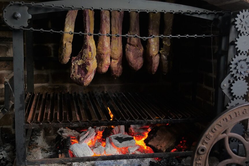 Big tomahawk steaks hang in an open fire bbq