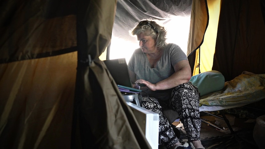 Woman on a laptop inside a tent.